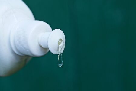 part of a white plastic bottle with a drop of shampoo on a green background