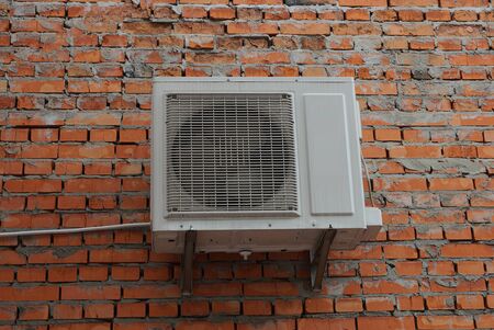 one white big fan hanging on a red brick wall of a building on the streetの写真素材