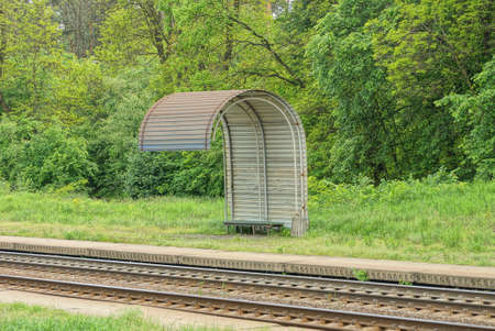 gray empty old metal stop by the railway against a background of green grass and vegetation