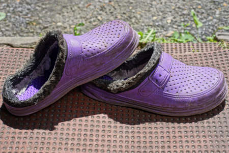 old lilac plastic slippers stand on a brown doorstep in the street