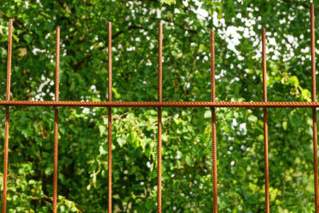 part of an iron fence made of red rusty iron bars on the street against a background of green vegetationの写真素材