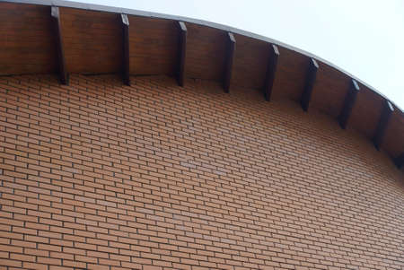 part of the house with a brown brick wall and a roof with wooden boards and formwork against a gray...