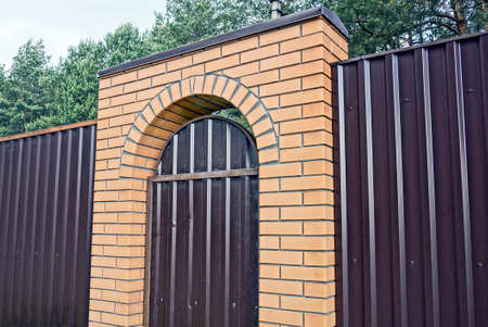 brown metal fence wall with closed door and brick arch on the streetの写真素材