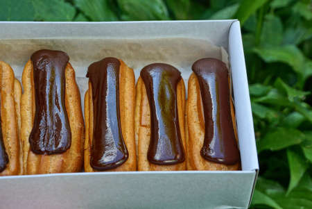 brown cakes in chocolate lie in a white paper box against a background of green vegetation