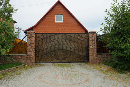 brown metal gate with a black forged pattern in front of a red private brick house with a window