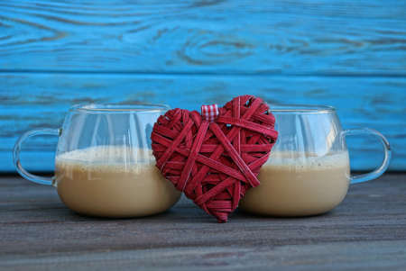 two glass cups with brown coffee and a red heart stands on a black table against a blue wall...