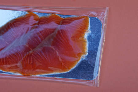 pieces of red fish in a gray plastic transparent packaging lie on an orange table