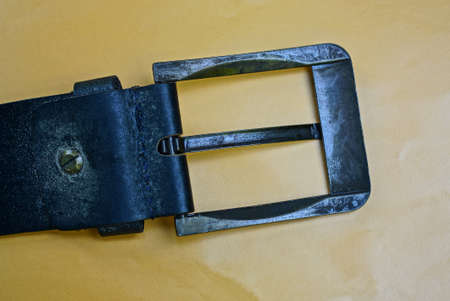 part of black old leather belt with metal plaque on brown background