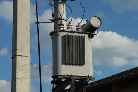 one gray metal transformer on a pole with electric wires against a blue sky