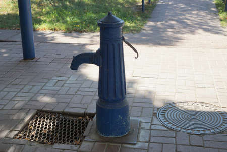 one old blue iron crane pump stands on a gray sidewalk in the street