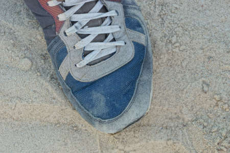 one old and dirty colored sneaker with white lace stands on gray sand in the streetの写真素材