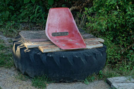 old red plastic chair on wooden planks and black car tire among green grass and vegetation in natureの写真素材
