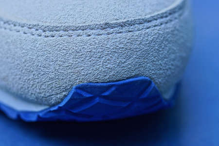 part of one white suede and plastic sneaker on a blue tableの写真素材