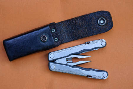 gray metal multitool and black leather case lie on the brown table