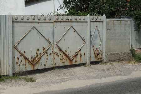 old rustic iron gate in brown rust on the street by an asphalt road