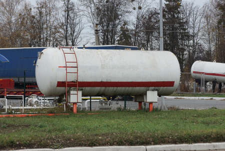 one white large iron tank at a gas station stands in the green grass