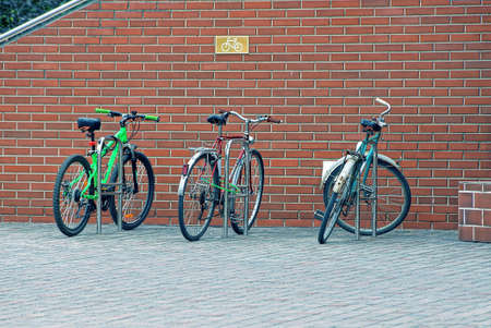 three bicycles are parked on the street against a brown brick wall