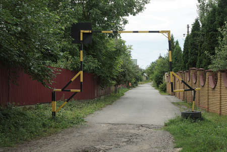 striped iron barrier on an asphalt road and in green grass in front of a brick fence on the street