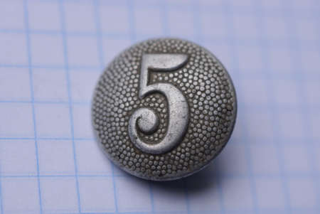 one old gray button with number five on a white paper