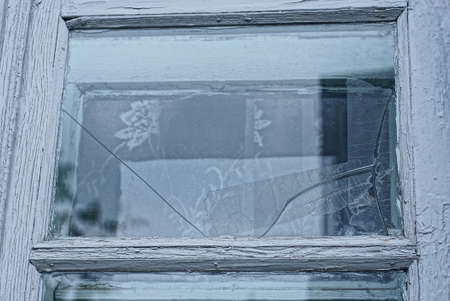 part of an old window with a white wooden frame and gray glass with cracks