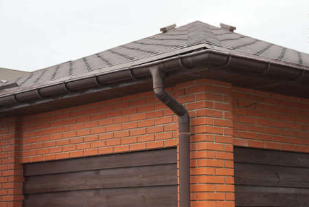 house facade made of red bricks and brown wooden planks under a tiled roof with a plastic drain pipe