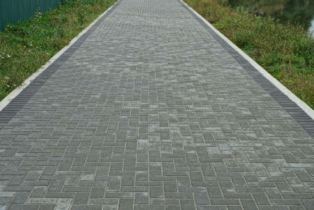 alley of gray paving slabs along the green grass on street