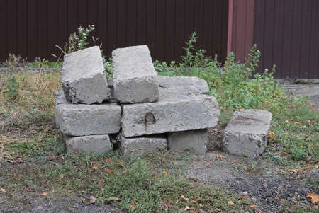 a pile of old gray concrete blocks lie on the ground and in green grass outside near a brown fence...