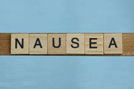 gray word nausea in small square wooden letters with black font on a blue backgroundの写真素材