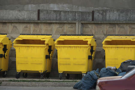 a row of yellow plastic dumpsters along a gray concrete wall outside