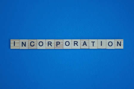 gray word incorporation in small square wooden letters with black font on a blue background