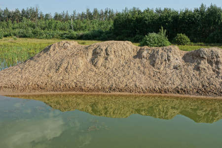 part of the lake with green water and a pile of brown sand on the shore against the background of...