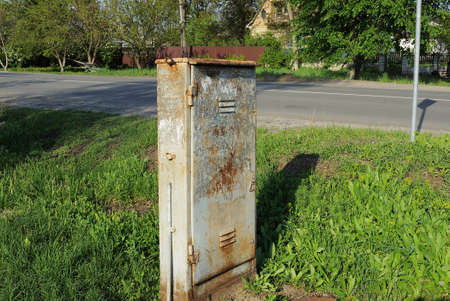 one old closed metal box for electrical wires in brown rust outside in green grass