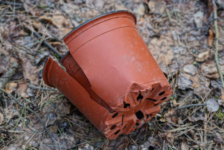 garbage from one brown broken plastic flowerpot with a crack lies on the ground and fallen leaves in...