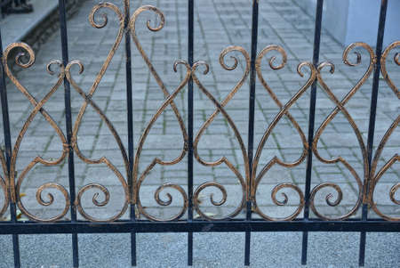 metal texture from a brown forged pattern on black bars of a fence on the street against a gray...