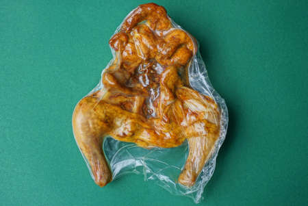 food from a piece of brown fried chicken in a sealed transparent plastic package lies on a green...