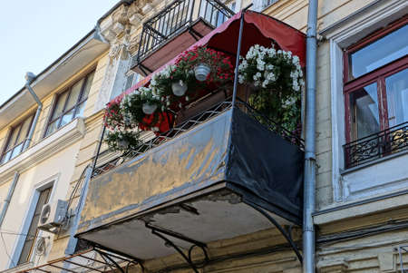 one black open balcony with a row of flowerpots with decorative flowers on a large wall of a house with windows outsideの写真素材