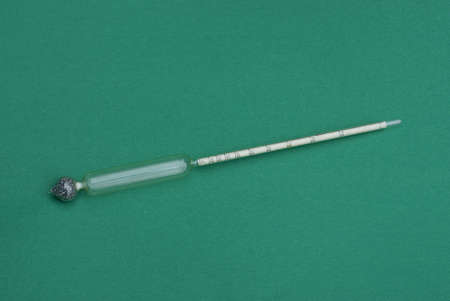 one old gray long glass alcohol thermometer lies on a green table