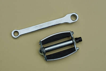 two bicycle parts made of gray metal knee and pedal lie on a brown table