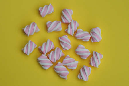 Many colored pink white candy marshmallows lie on a yellow table