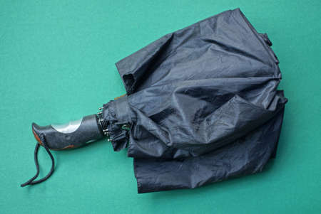 one black folded umbrella lies on a green tableの写真素材