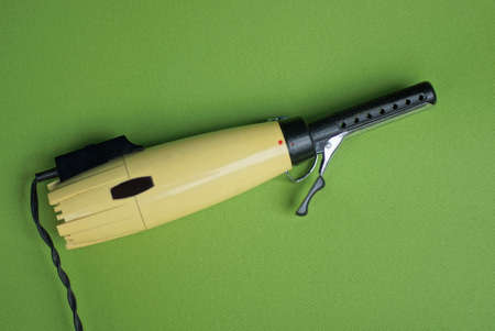 one old yellow hair dryer with a black metal curling attachment lies on a green table