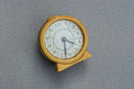one old yellow alarm clock with a white dial lies on a gray table