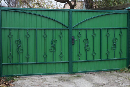 large closed green metal gate with wrought iron pattern on the street