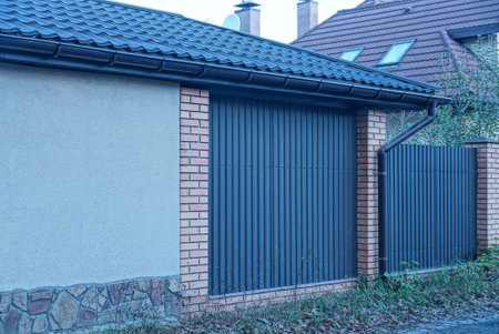 gray concrete wall of a private house under a tiled roof and part of a brown brick and metal fence...