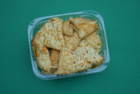 food from brown pancakes and pies in a white plastic bowl stands on a green table