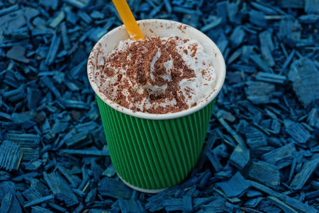 one large green paper cup with a cappuccino drink with white creamy foam with brown chocolate stands on a blue backgroundの写真素材