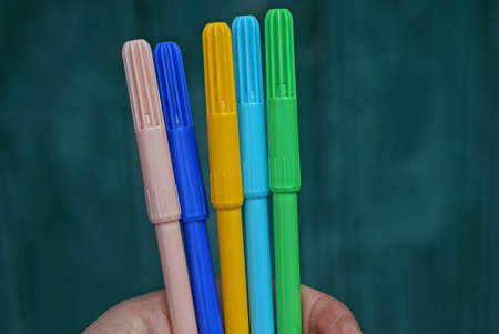 hand holds many colored plastic markers on green background