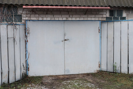 gray facade of an old garage with closed iron gates and part of a fence on the streetの写真素材