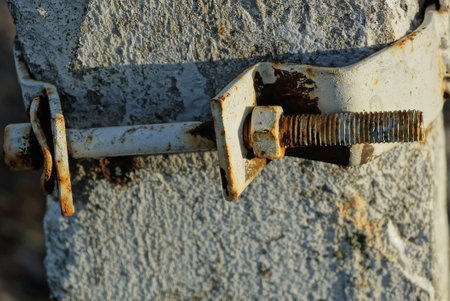long gray iron bolt with a nut in brown rust on a metal bracket on a concrete postの写真素材