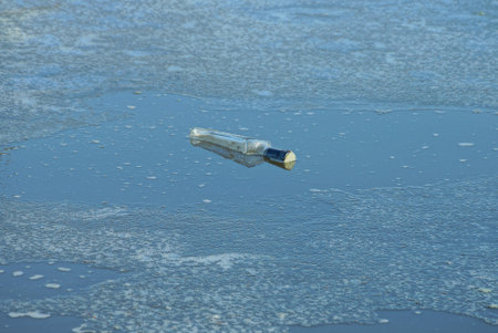 one large glass bottle in water among the gray ice of a winter reservoirの写真素材